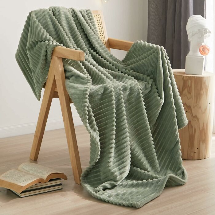 Cozy chair draped with a sage green textured blanket, capturing the essence of 2025 interior trends.