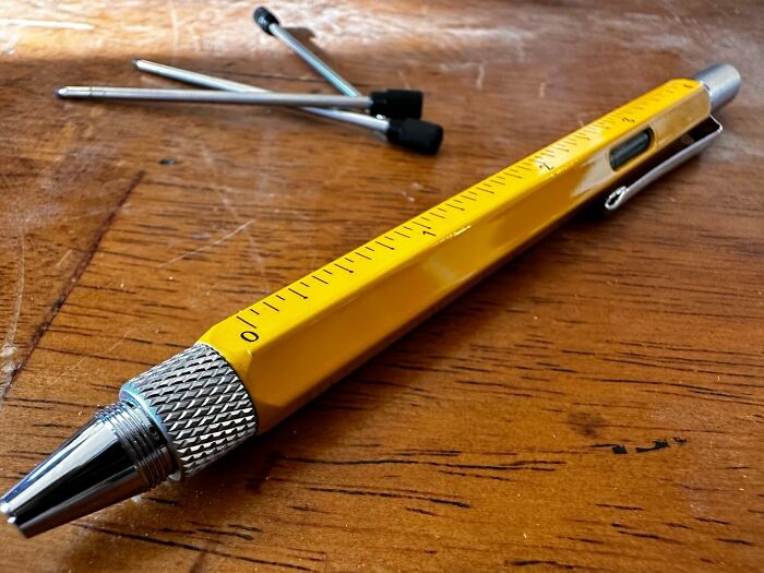 Yellow multi-tool pen with a ruler, level, and extra refills, on a wooden surface.