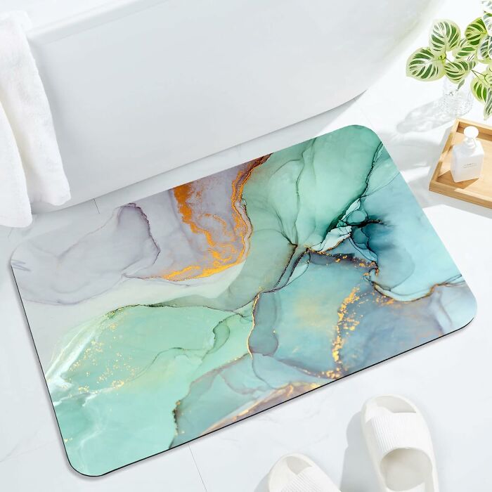 Abstract bathroom mat with teal and gold accents on white tiled floor beside bathtub, slippers, and plant, enhancing bathroom mats style.