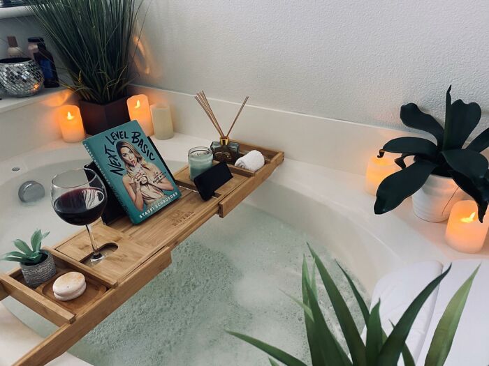 Relaxing bathtub scene with candles, plants, book, and wine glass showcasing affordable luxury finds on a humble budget.