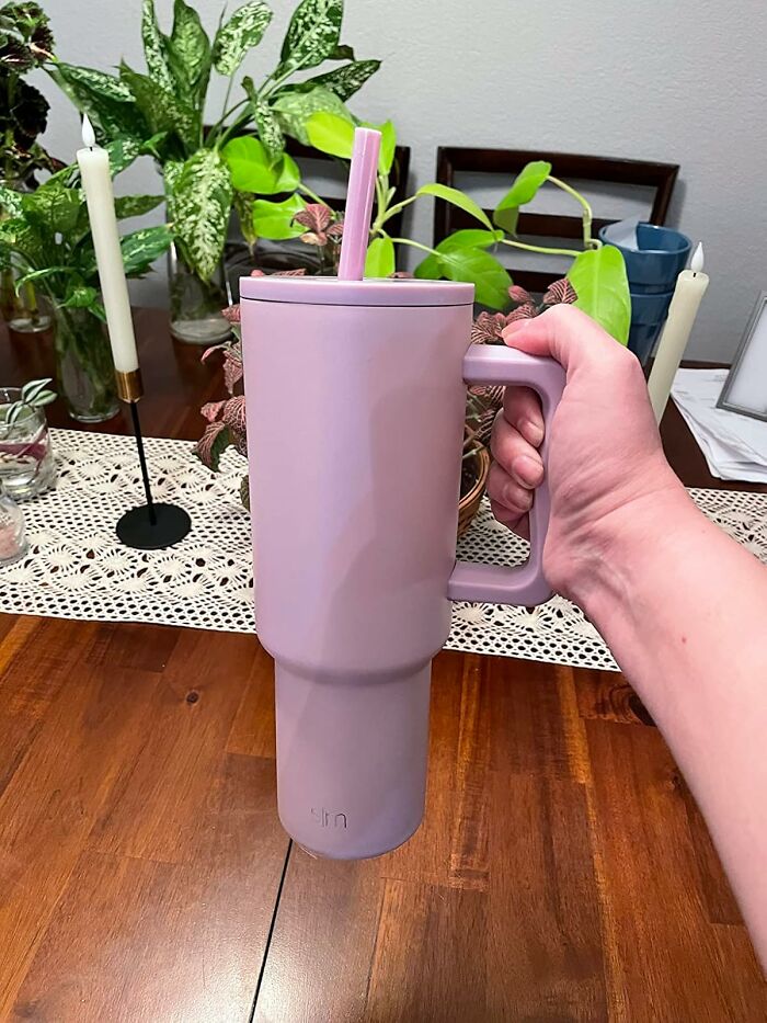 Aesthetic pink tumbler held by a hand, surrounded by decorative plants on a wooden table.