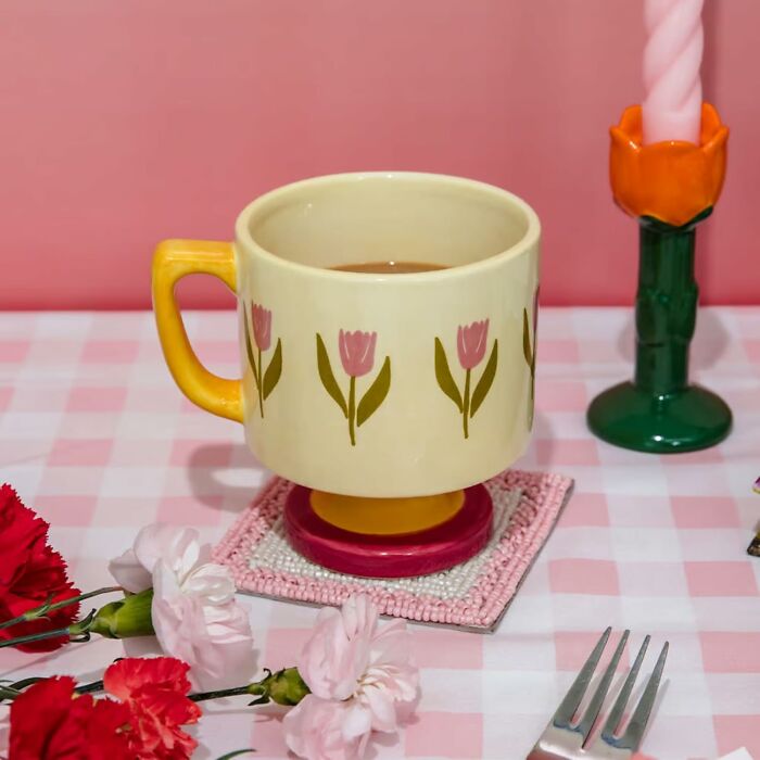Colorful cup from Bando with floral design on a checkered table beside flowers and a candle.