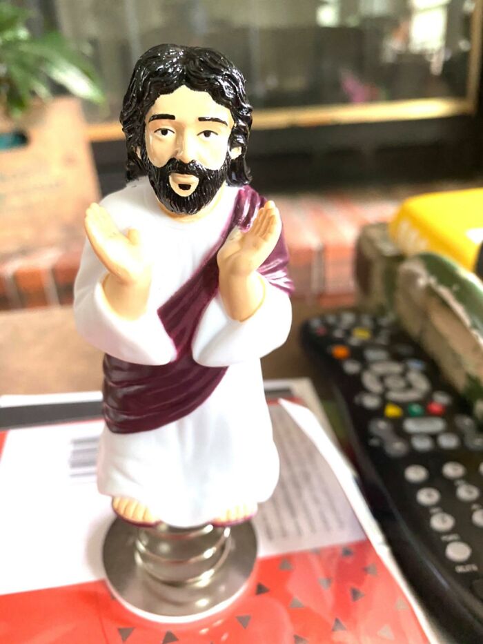 Archie McPhee item depicting a bearded figure in a robe, with hands raised, on a table with a remote nearby.