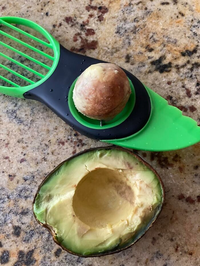 Avocado slicer demonstrating its worthiness by neatly cutting an avocado in half on a granite counter.