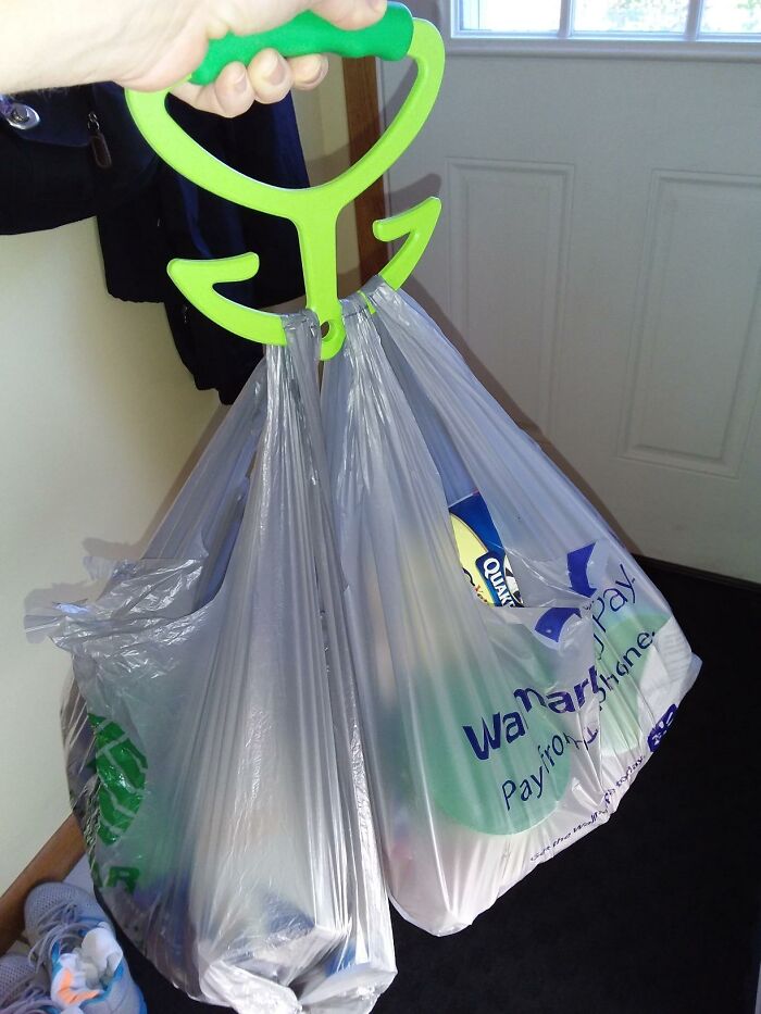 Hand holding a green shopping bag carrier with two loaded plastic bags, showcasing clever inventions for convenience.