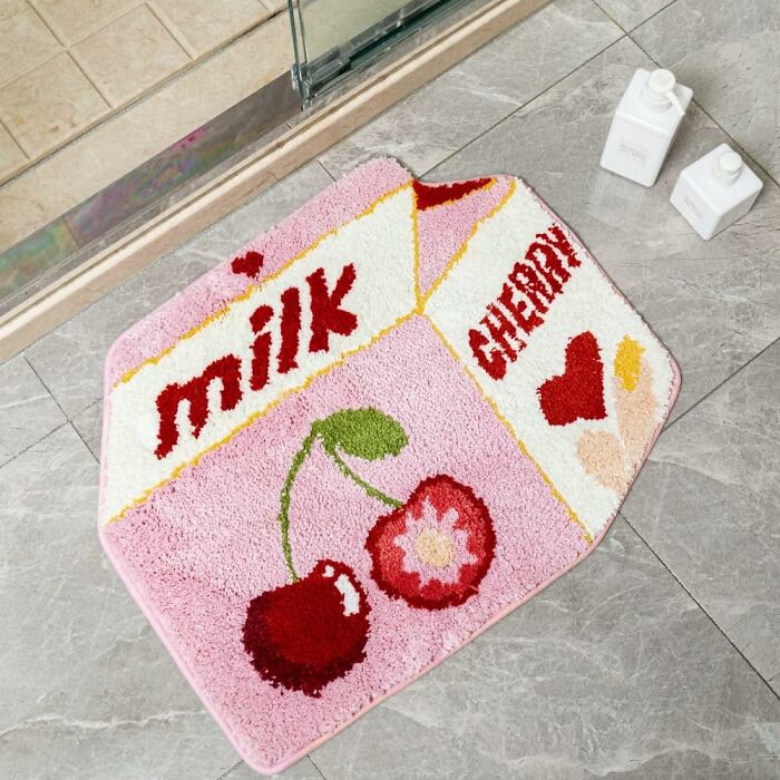 Pink cherry and milk design bathroom mat on gray tile floor next to glass shower and white pump bottles.