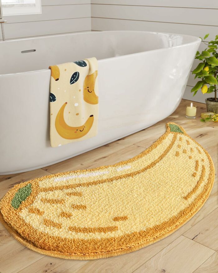 Yellow banana-shaped bathroom mat on wooden floor next to white tub, enhancing bathroom mats style and decor.