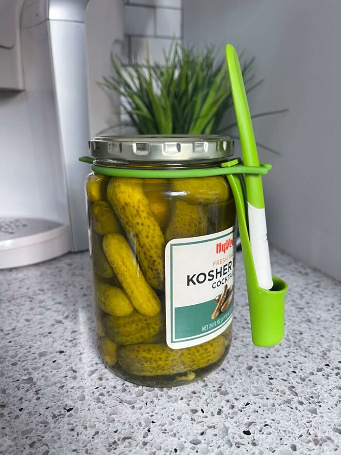 Jar of kosher pickles with a green holder on a countertop, showcasing a cult favorite.