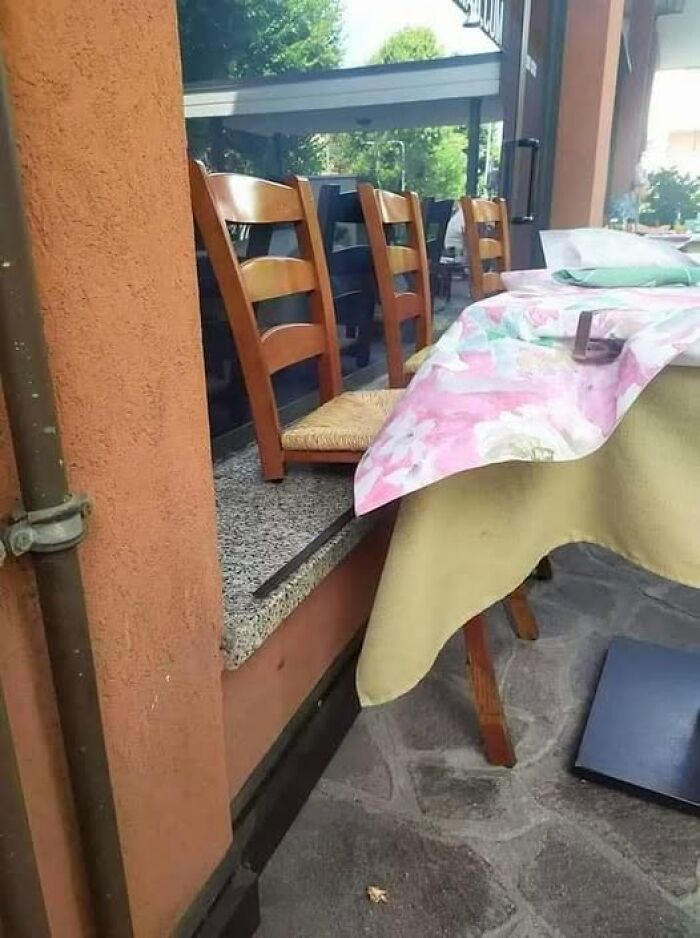 Chairs partially tucked under a floral tablecloth on a ledge, creating a weird visual illusion.