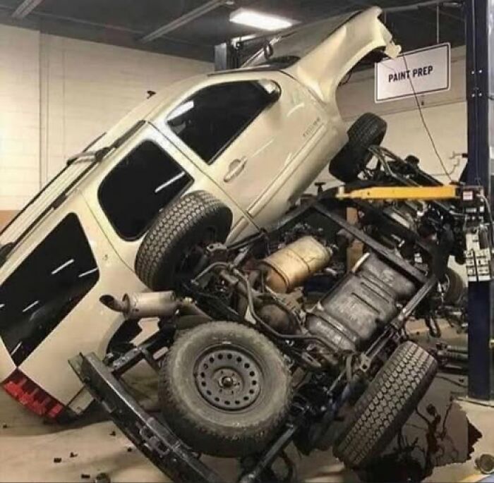 Weird image of an upside-down car in a repair shop, showcasing a chaotic scene in the paint prep area.