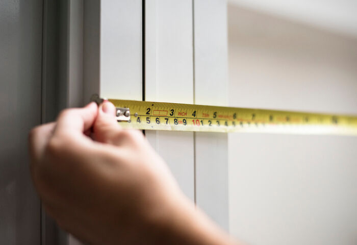 A hand using a tape measure on a door, illustrating American norms.