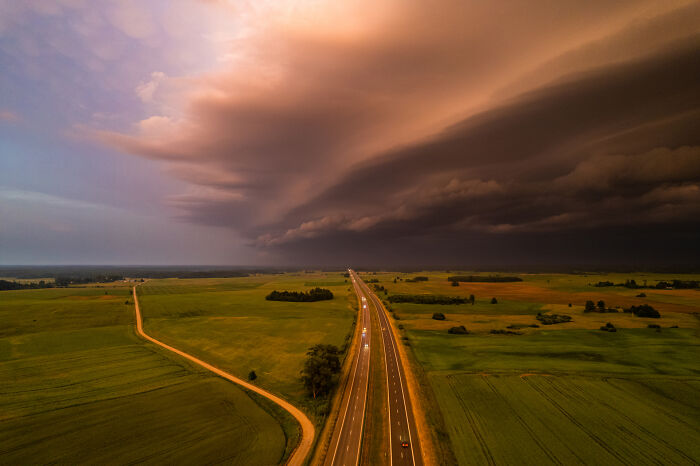 Aerial view of a stormy sky over a Lithuanian highway and green fields.