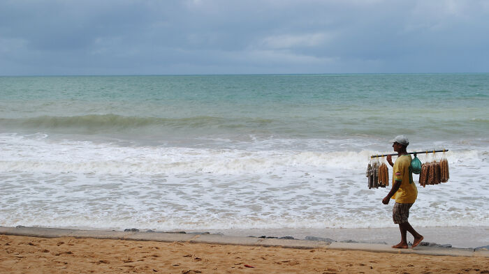 Vendor walking on a retro Brazilian beach with ocean waves and cloudy sky in the background.