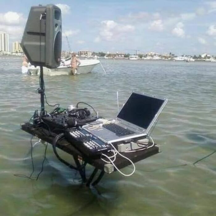 DJ equipment on a table submerged in water, with a speaker and laptop, showcasing a weird image in a unique context.