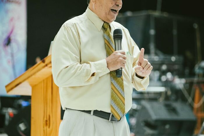 Man in a yellow shirt holding microphone, gesturing during a speech, related to songs as ringtones concept.