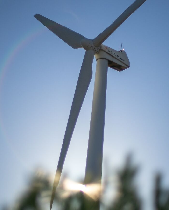 Wind turbine against a clear sky, part of 'The Coincidence Project' by Denis Cherim, sunlight creating a halo effect.