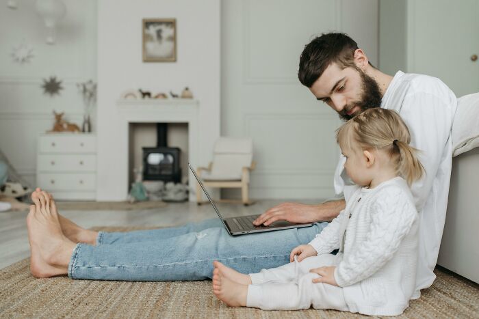 Man working on a laptop at home with his child, showcasing the best perks of not having to go to the office.