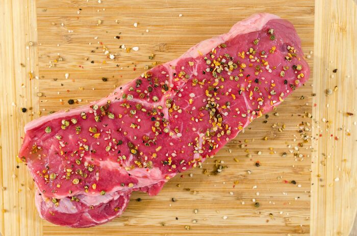 Raw steak seasoned with pepper on a wooden board, related to fitness myths about protein sources.