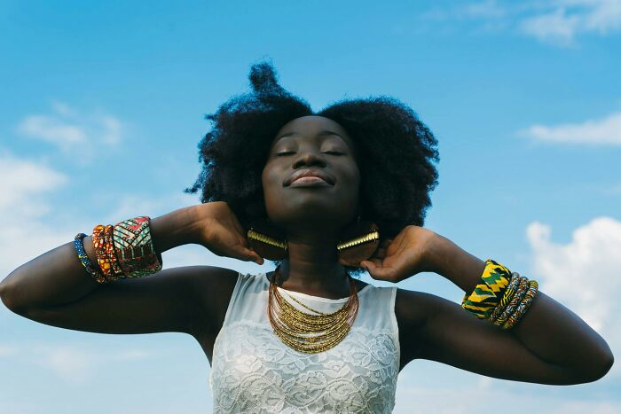 Woman embracing change mindsets, wearing colorful jewelry and a white top, standing against a blue sky background.