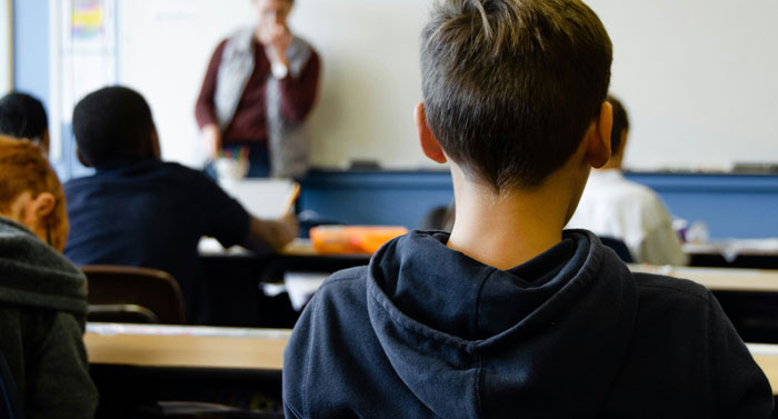 Estudiante en clase mientras el profesor habla, capturando un momento divertido durante la lección.