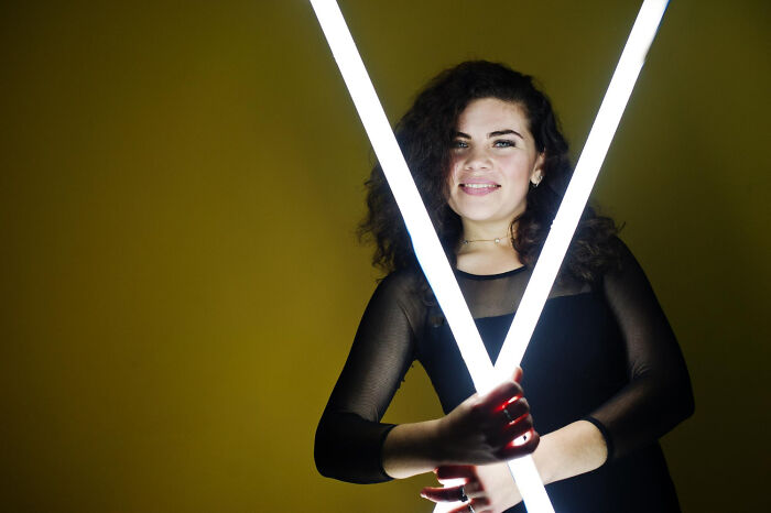 Woman holding two light tubes in a "X" shape against a yellow background, representing unique individual impact.