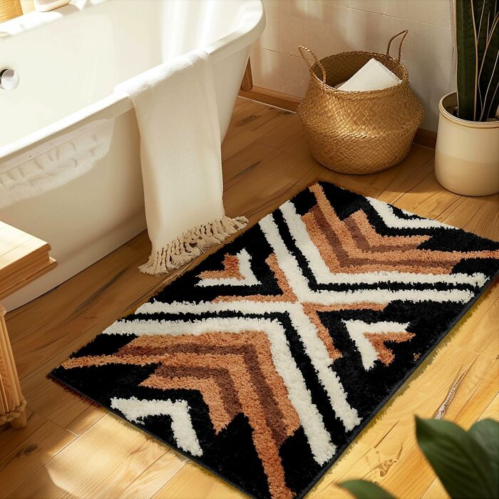 Geometric patterned bathroom mat on wooden floor next to a bathtub and woven basket with towel.
