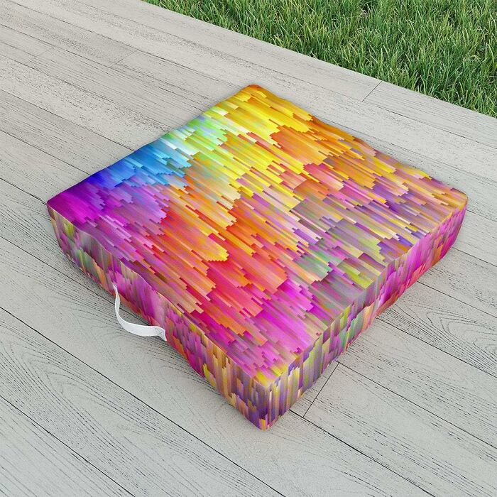 Colorful geometric outdoor seat cushion from Society 6 on wooden deck next to green grass.