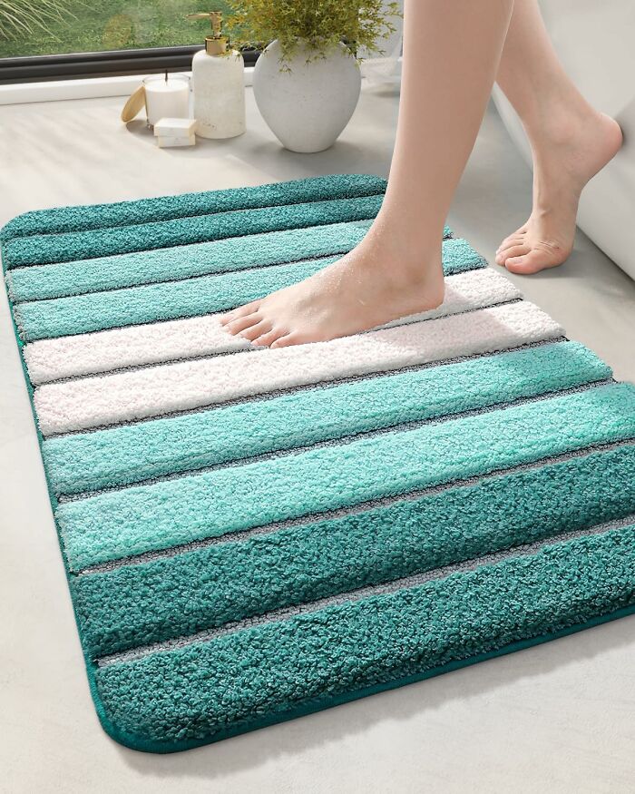 Person stepping onto a teal and white striped bathroom mat on a light floor with decorative plants nearby.