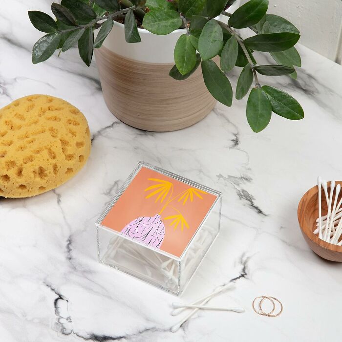 Decorative storage box from Society 6 on a marble surface with a plant, sponge, and cotton swabs.