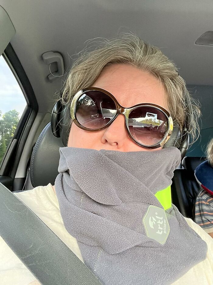 Person in sunglasses wearing a compact travel pillow in a car, ideal for minimalist carry-on packing.