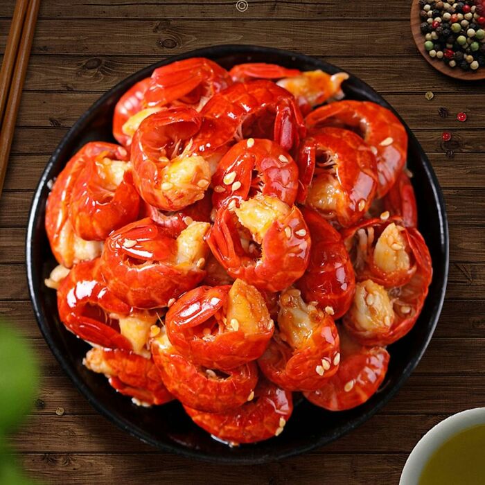 Vibrant snack of glazed shrimp with sesame seeds on a black plate.