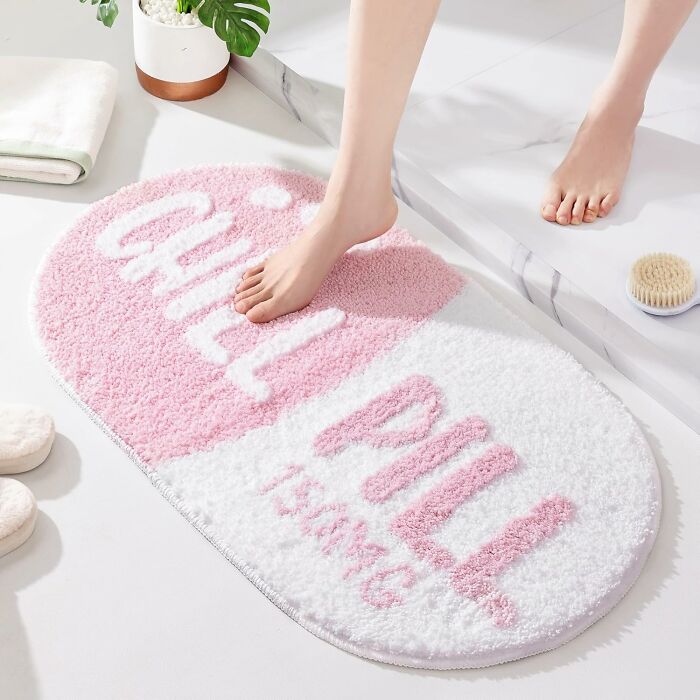 Foot stepping on a pink and white bathroom mat with chill pill design, enhancing bathroom mats style and comfort.