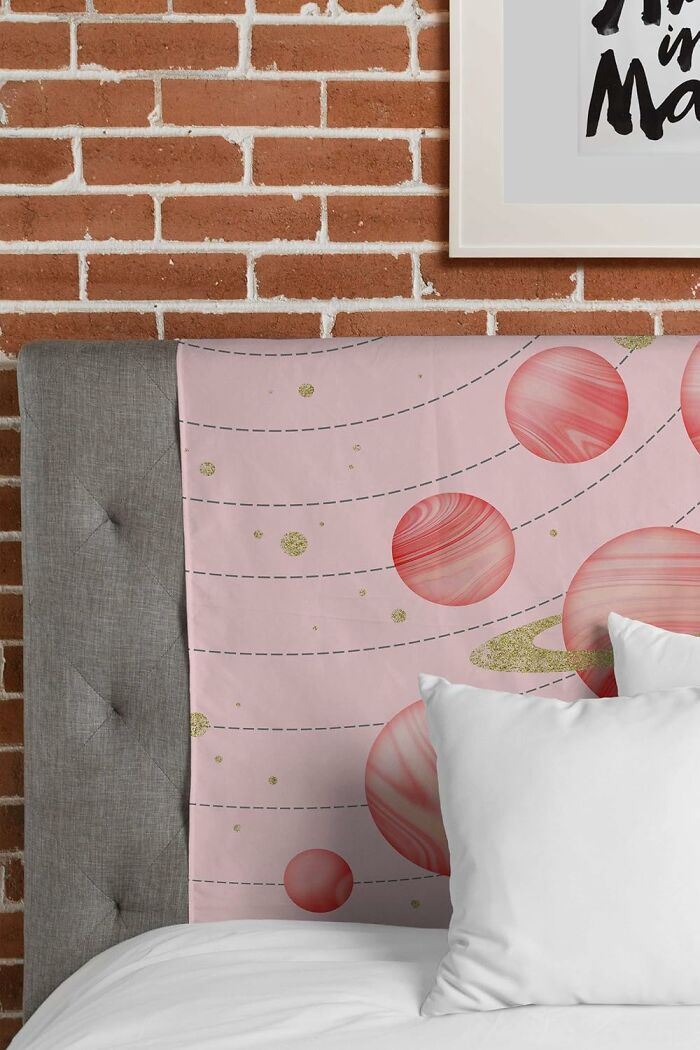 Society 6 tapestry with pink planets design on a gray headboard against a brick wall.