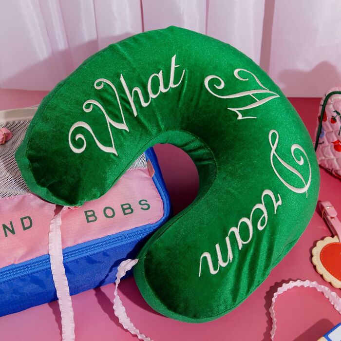 Green Bando neck pillow with "What a Dream" text, placed on a pink surface with a colorful bag.