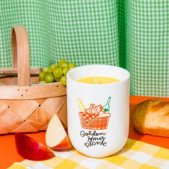 Bando candle with "Golden Hour Picnic" design, beside fruit and a basket.