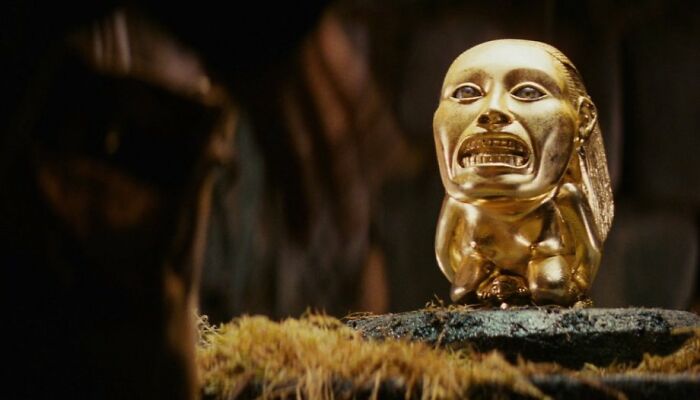 Golden idol movie prop on a mossy pedestal from a famous film.