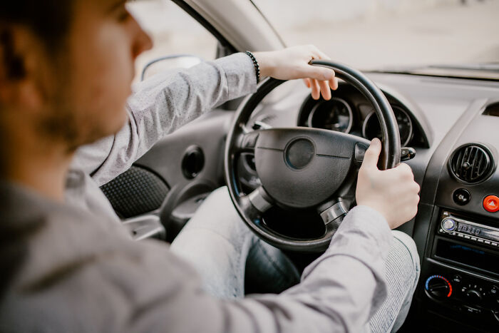 Young man driving a car holding the steering wheel with both hands focused on the road ahead inside the vehicle.