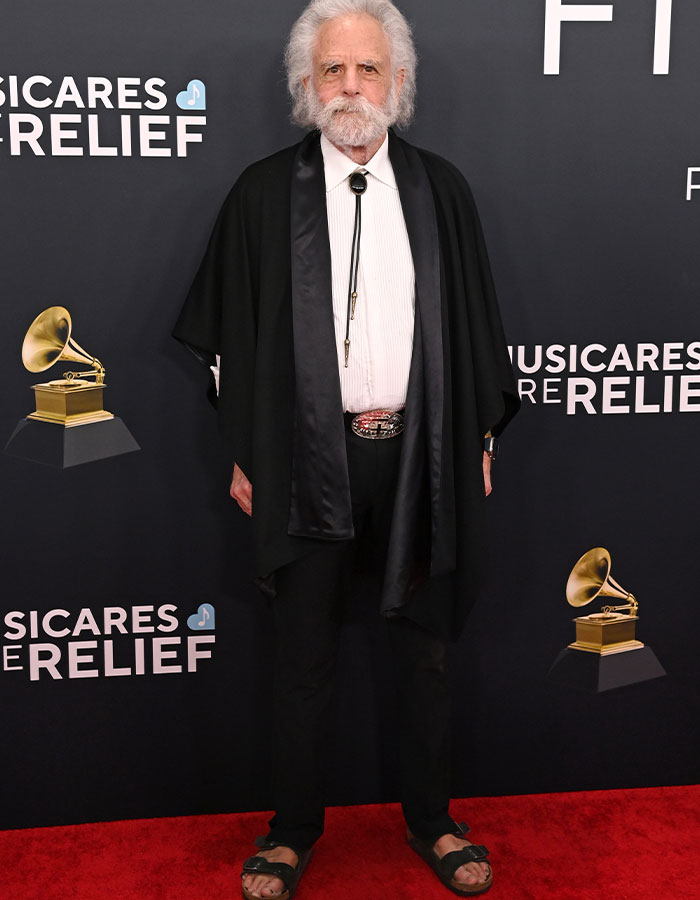 "Man in black cape on red carpet at 2025 Grammys, standing in front of MusiCares backdrop."