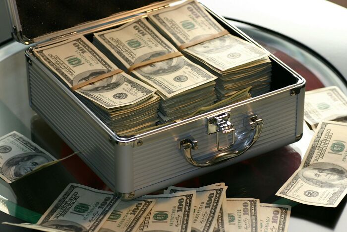 Stacks of cash in an open briefcase on a table, symbolizing dumb rumors about wealth.