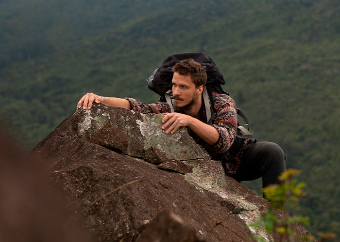 Man climbing a steep rocky slope with a backpack, showcasing one of the scariest hikes.