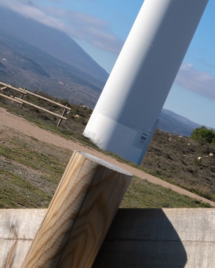 Contrasting perspective of a wooden post and wind turbine in a grassy landscape from the Coincidence Project series by Denis Cherim.