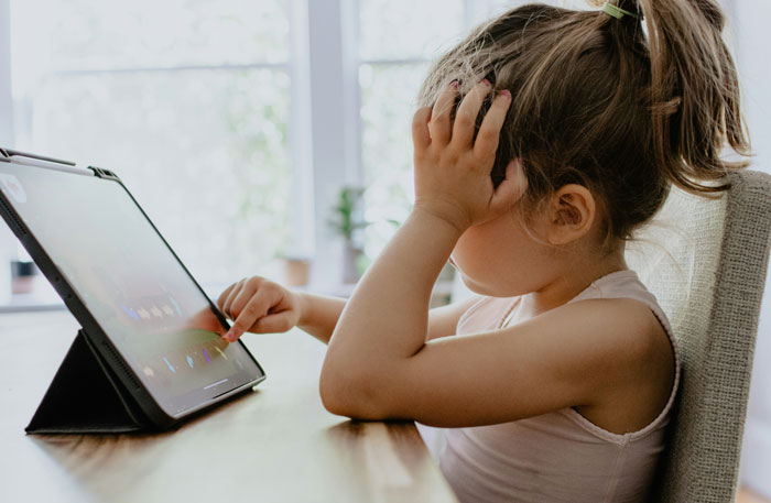 Child with frustrated expression using a tablet, illustrating a technique to raise entitlement-free kids.