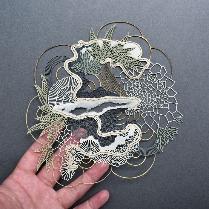 Intricate paper art design by Pippa Dyrlaga held in a hand, showcasing nature-inspired patterns on a gray background.