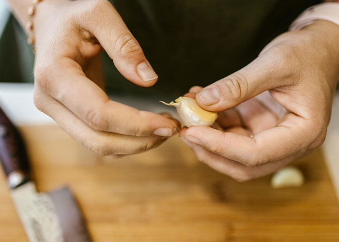 Hands peeling garlic on a wooden cutting board, adding a whimsical touch to cooking.