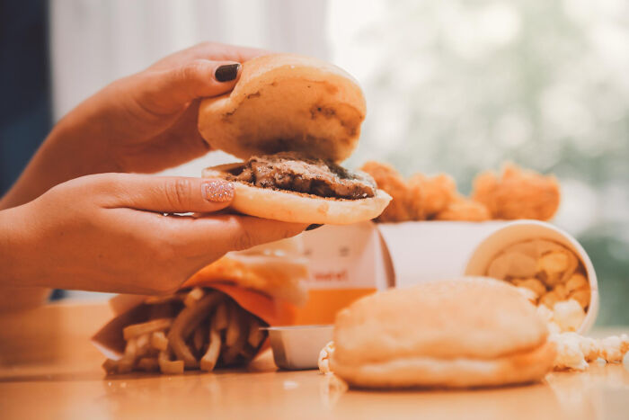 Person holding a burger with fries and popcorn on the table, reflecting common food experiences learned young.