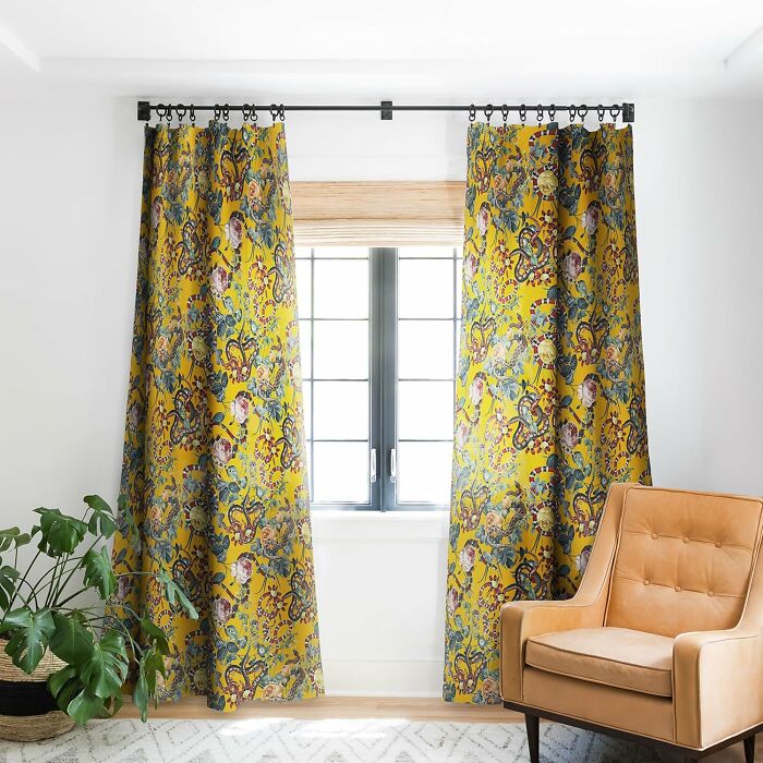 Patterned yellow curtains from Society 6 in a room with a tan chair and potted plant.