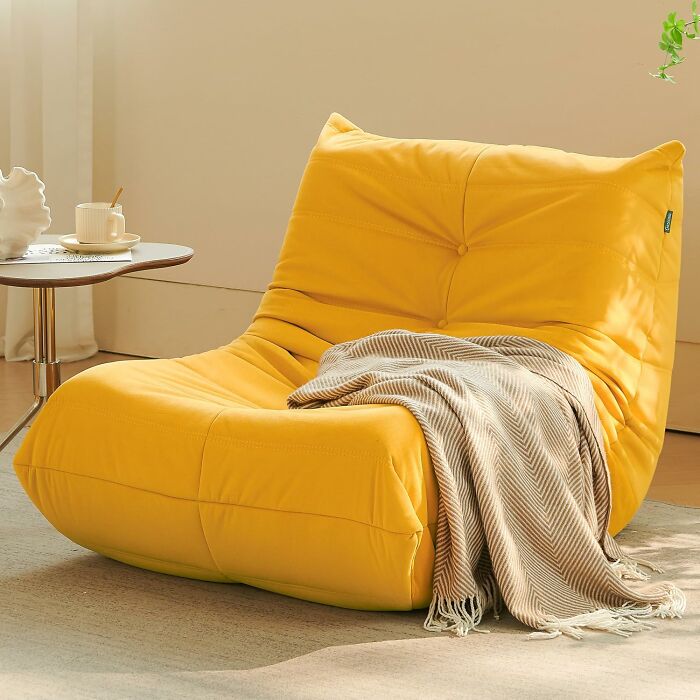 Cozy yellow lounge chair with a striped throw, reflecting 2025 interior trends, beside a small round table with a cup.