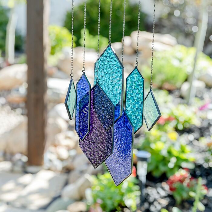 Colorful glass wind chimes hanging outdoors, reflecting sunlight.