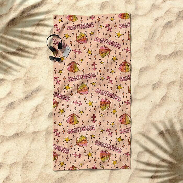 Sagittarius-themed Society 6 beach towel on sandy ground with sunglasses and headphones nearby.