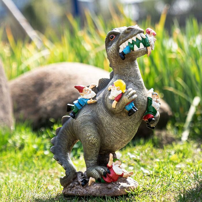 Dinosaur garden statue with gnomes, showcasing an impulse buy on grass.